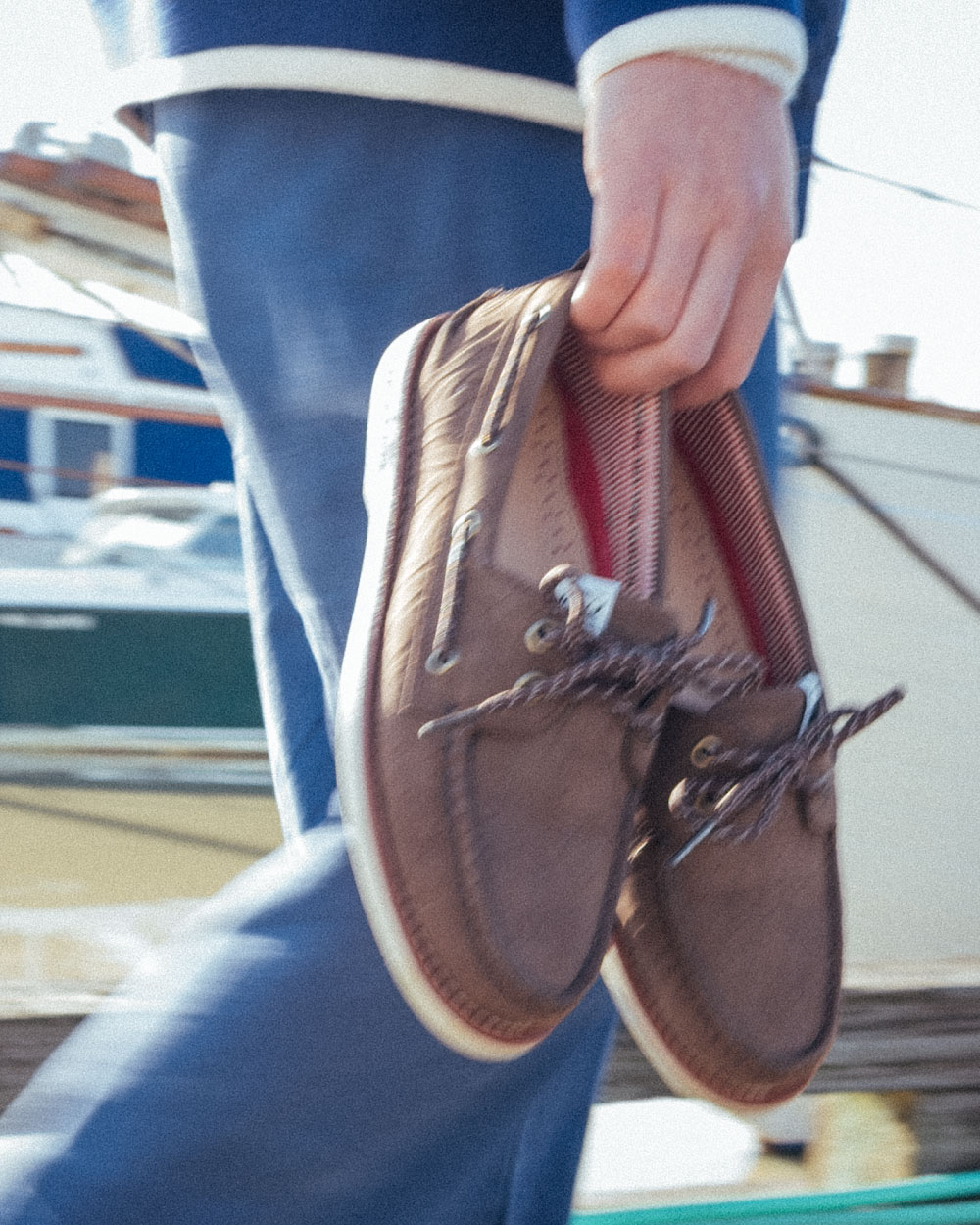 A person walking along a dock beside a sailboat with the Herschel Supply Company Authentic Original Lug Chukka Sperry shoes in Peacoat/Navy/Blanc de Blanc
